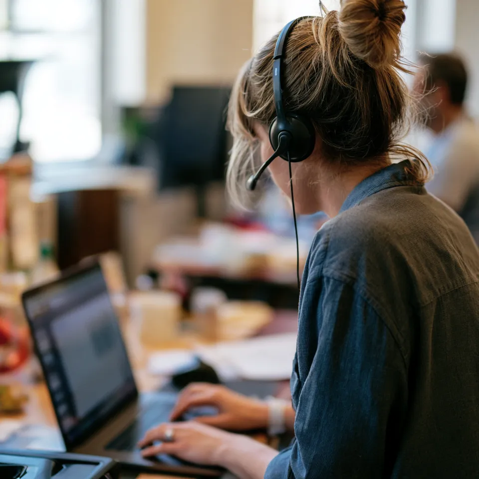 Over-the-shoulder view of a person with a headset typing on a laptop