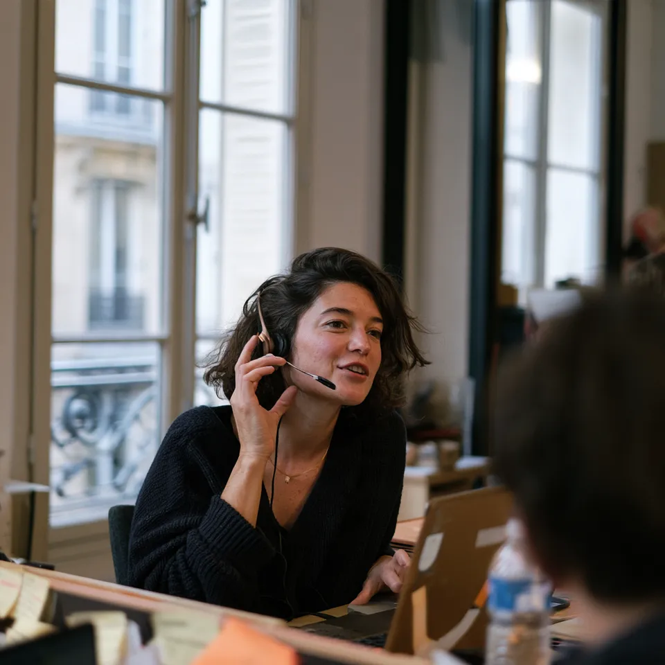 A woman with an office headset talking while looking at her laptop