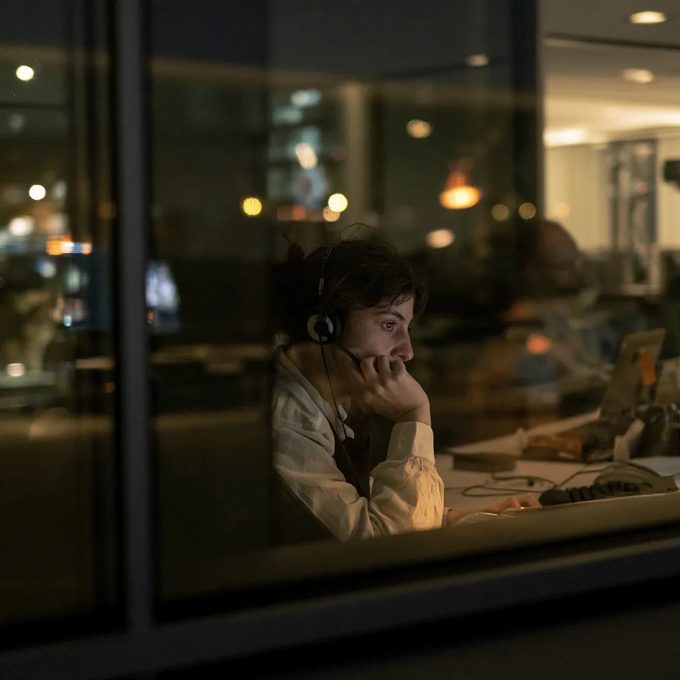 An agent with a headset seen through an office window at dusk